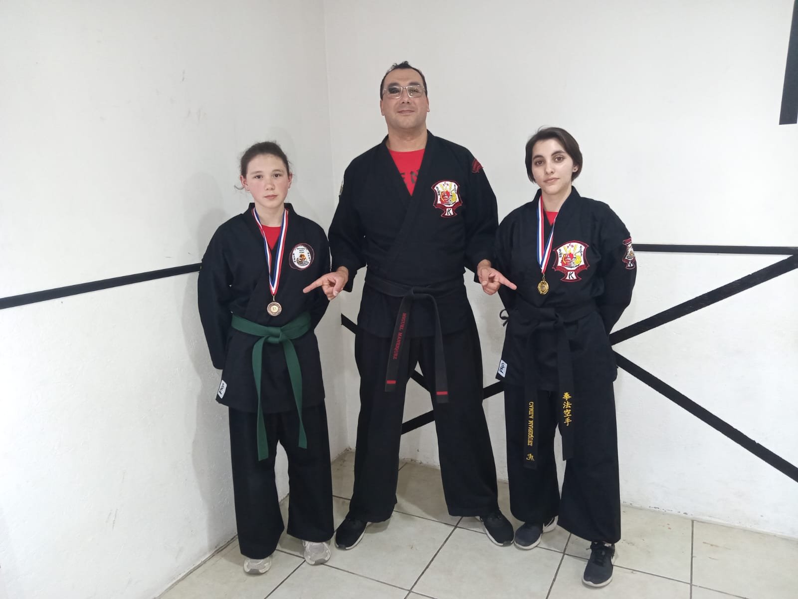 Dos alumnas con cinturón verde y negro junto a su instructor
